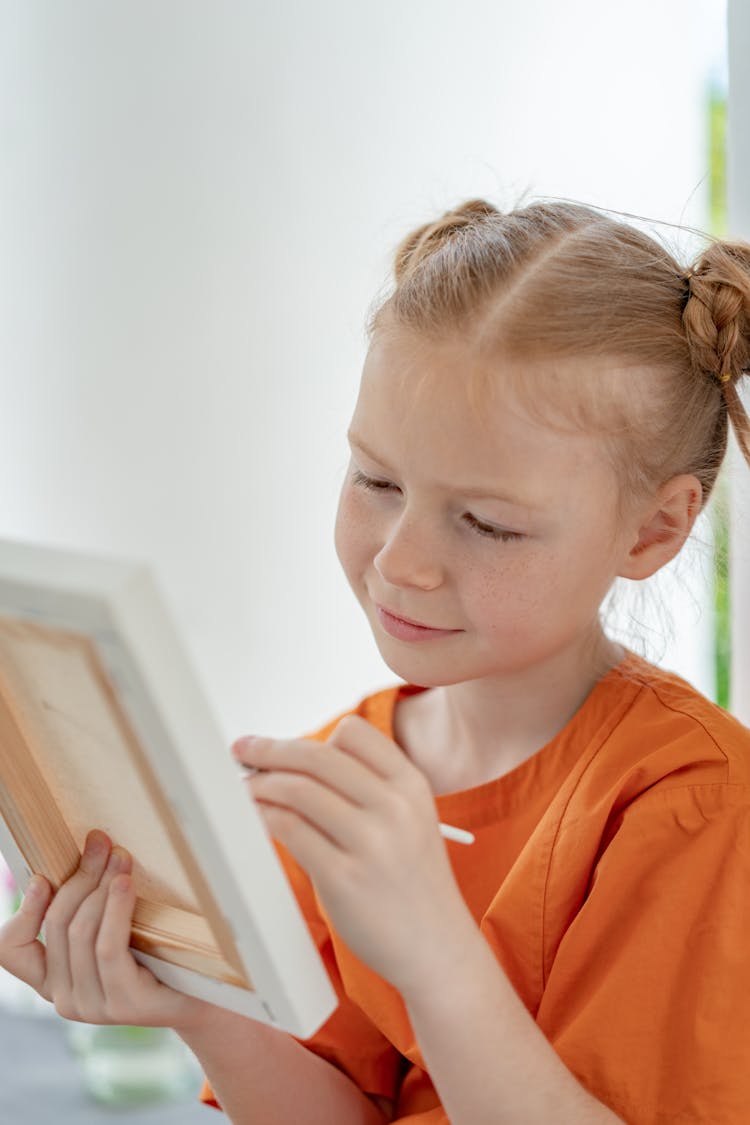 A Girl In Orange Shirt Holding A White Frame