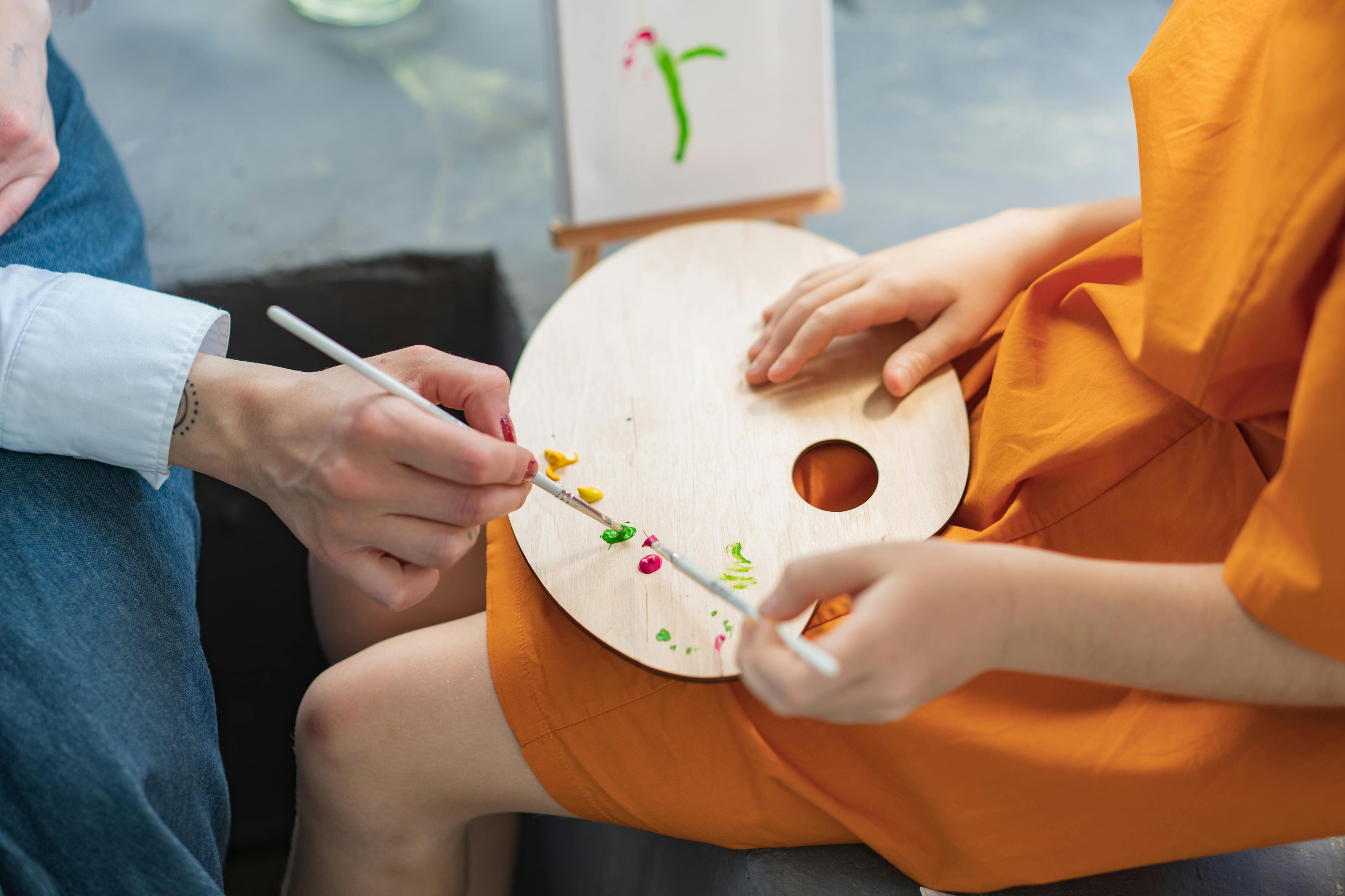 Creative close-up of hands painting using a palette and brush. Art creation at an indoor setting.