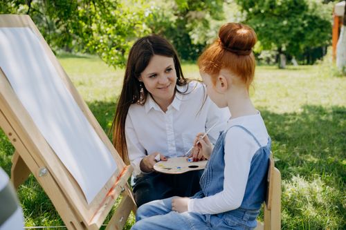 Free A woman guides a child in an outdoor painting lesson, fostering creativity and learning. Stock Photo