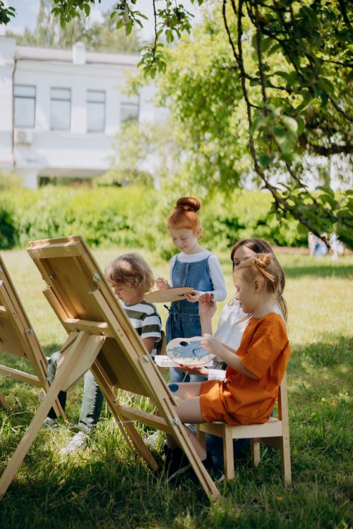 Free Group of kids painting in a park on a sunny day, surrounded by nature. Stock Photo