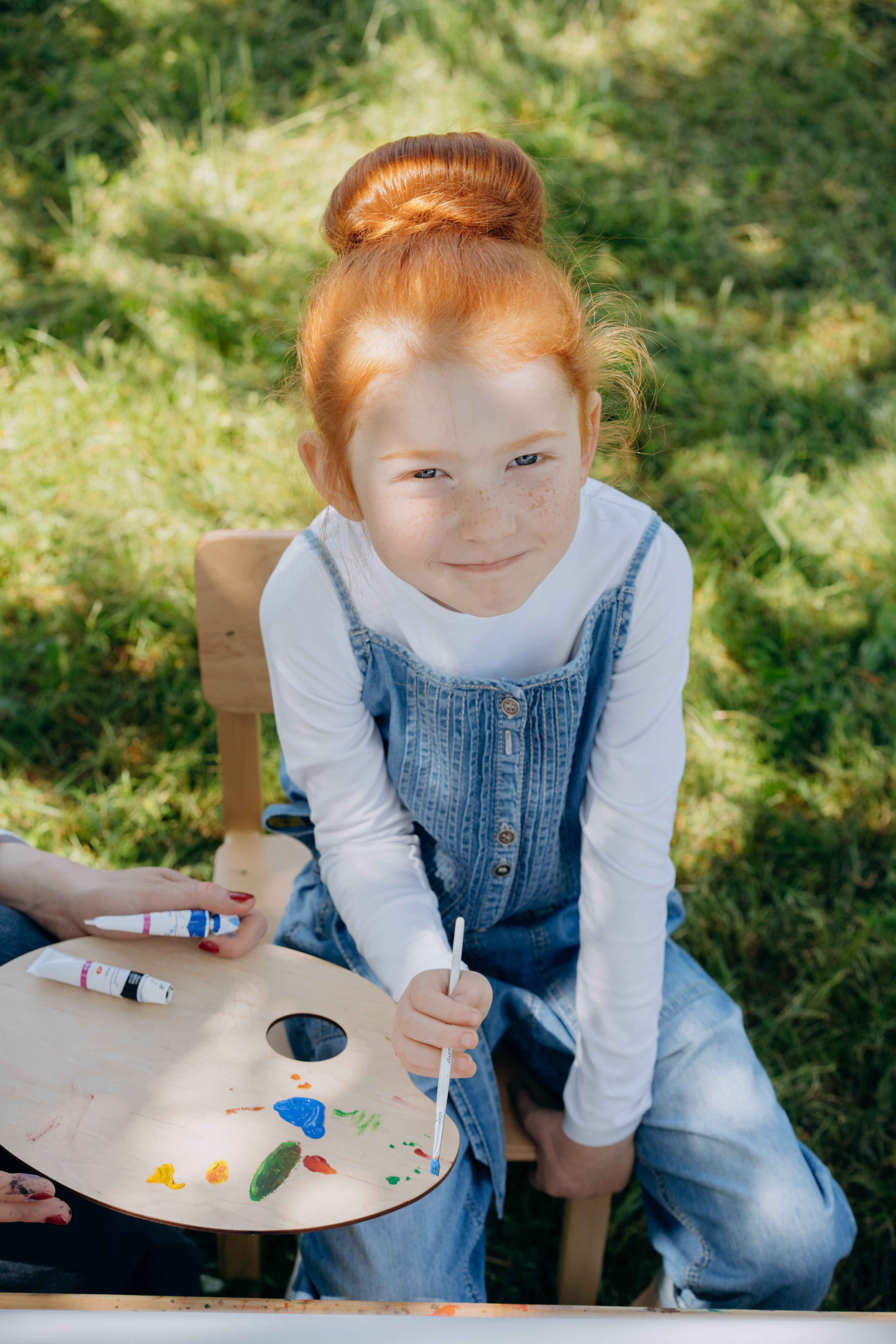 A young girl with ginger hair enjoys painting outdoors on a sunny day.