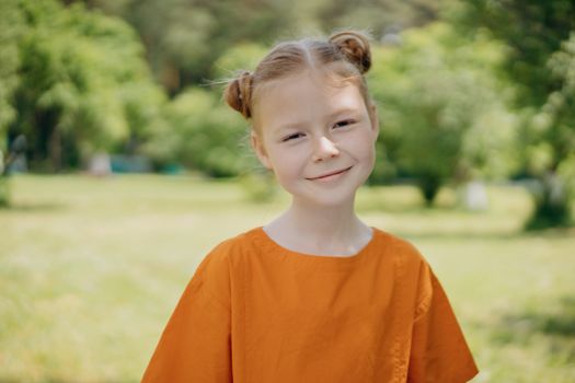 A cheerful girl in an orange shirt smiling in a sunny outdoor setting.