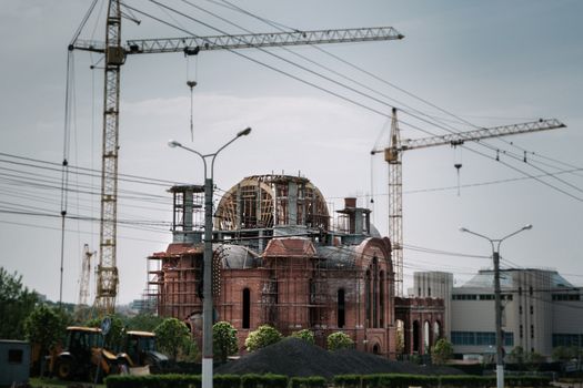 A city scene of a red brick building under construction with visible cranes.