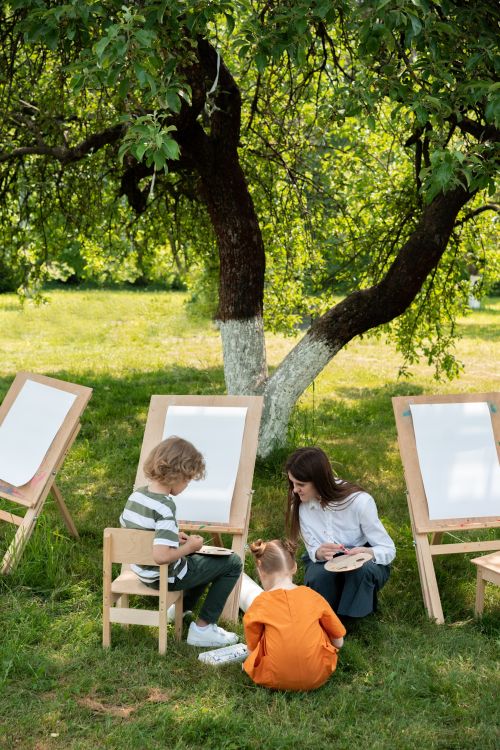 Free Children engaging in outdoor painting on a sunny day in a garden. Stock Photo