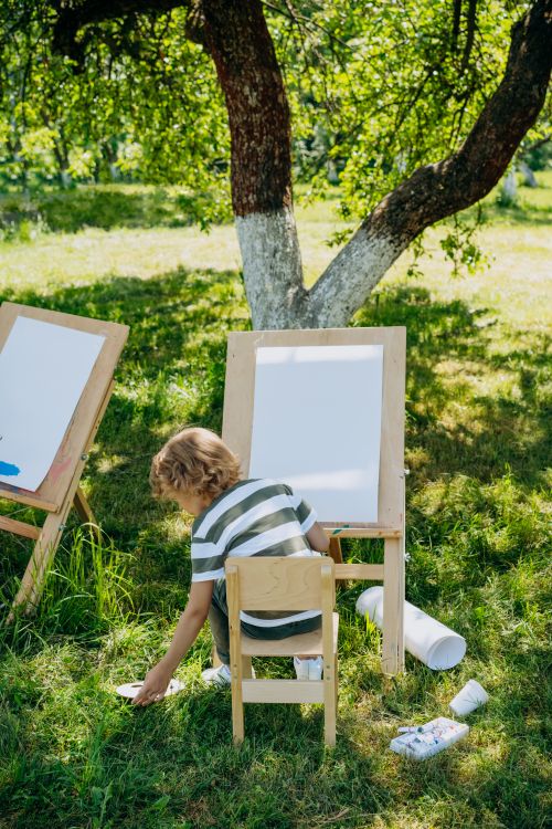 Free A young child painting on a canvas easel in a sunny garden. Stock Photo