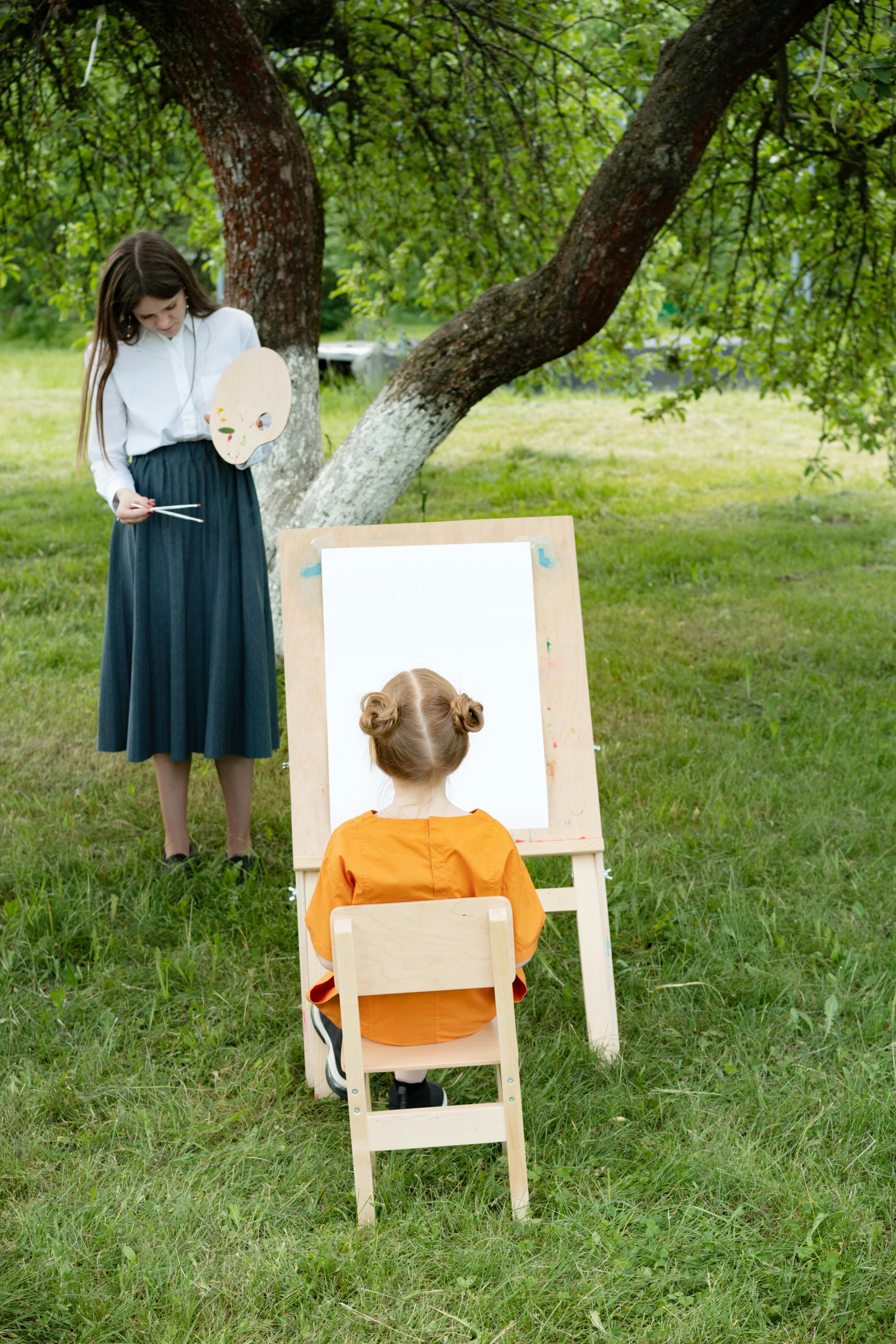 a woman teaching a child to paint while in the garden