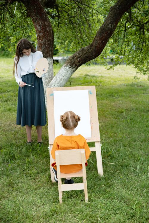 Free Girl in garden learns painting with teacher, capturing creativity in nature. Stock Photo