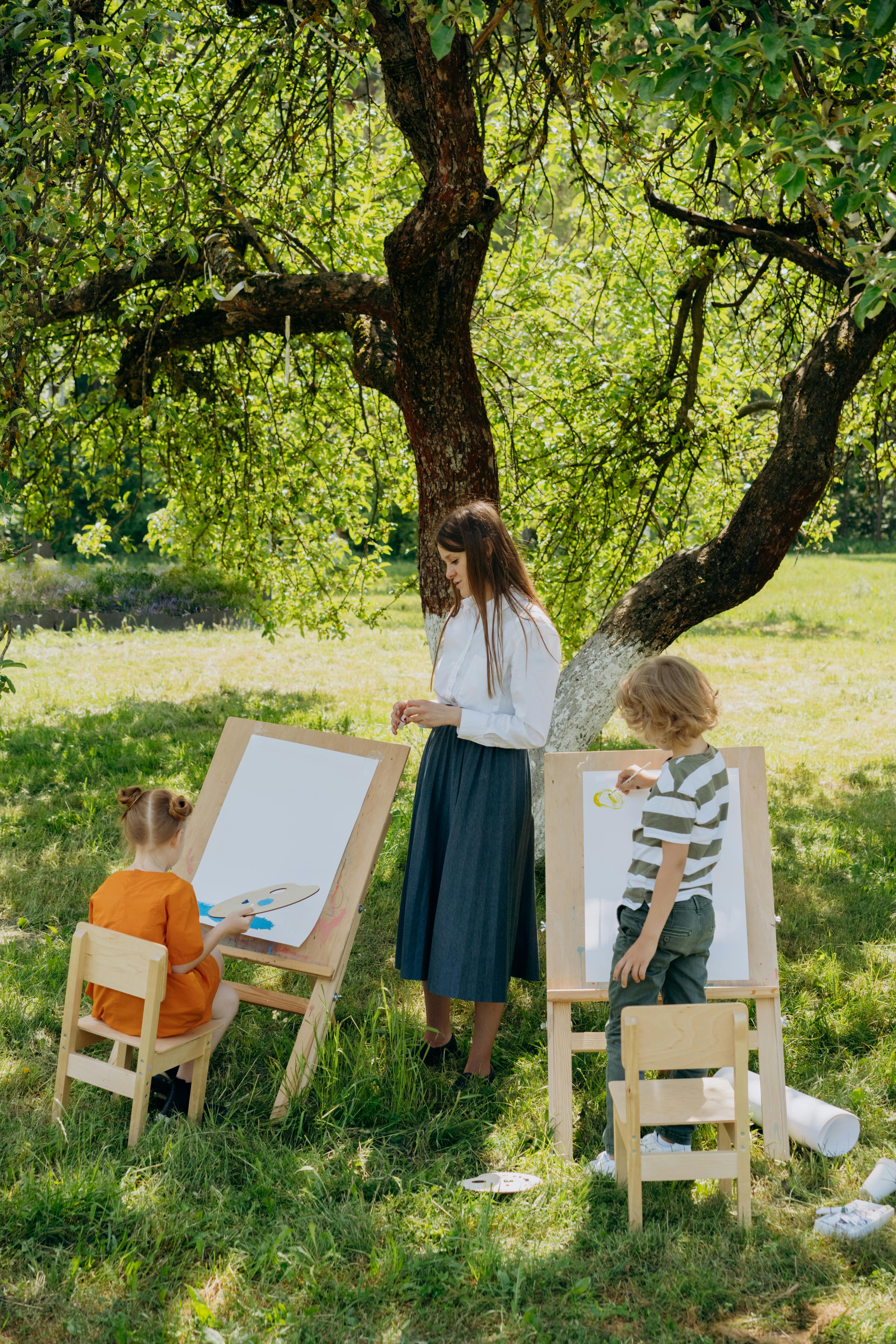 Children painting outdoors with a teacher, promoting creativity in nature.