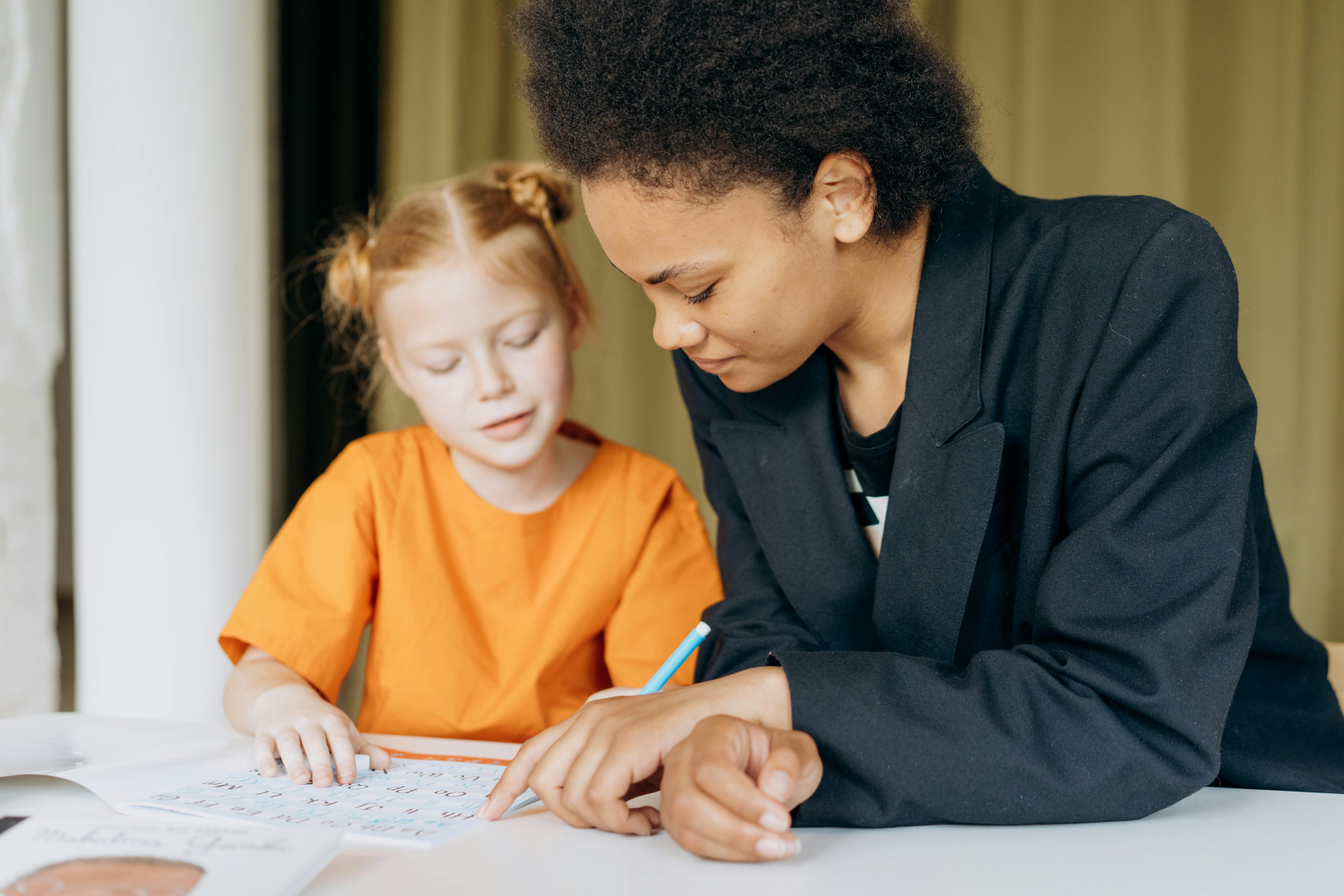 a girl writing on the workbook while sitting beside a woman in blazer