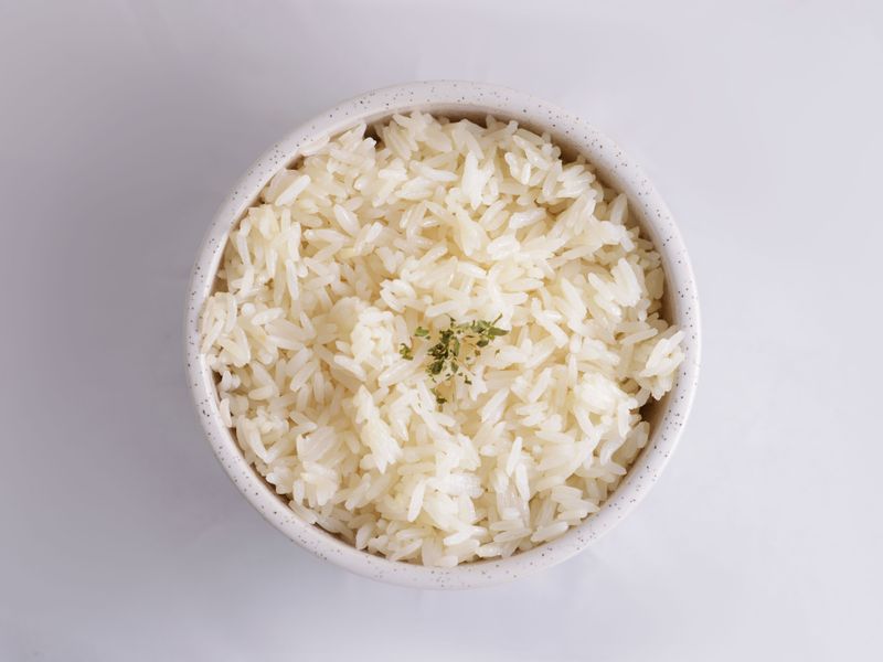 Close-up of cooked white rice in a bowl, garnished with herbs, in a minimalist setup.