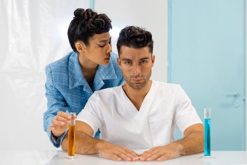 Free Woman Holding a Graduated Cylinder Behind a Man Stock Photo