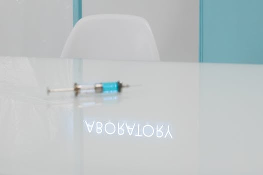 A syringe on a glass table with a laboratory reflection in a clean, clinical setting.