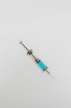 A vintage syringe with blue liquid on a white minimalist background.
