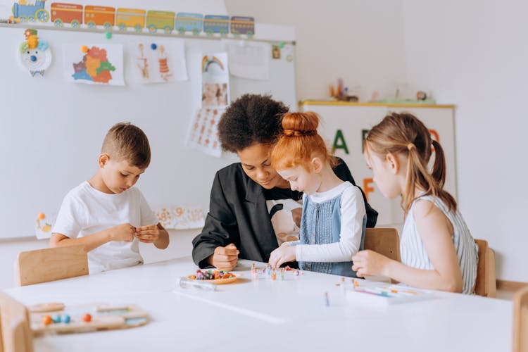 Children And Their Teacher Sitting At The Table