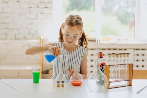 Free A girl conducting a science experiment with flasks in a bright classroom setting. Stock Photo