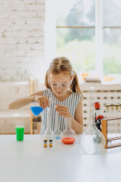 Free Young girl wearing goggles conducting a science experiment with colorful liquids at a home lab setup. Stock Photo