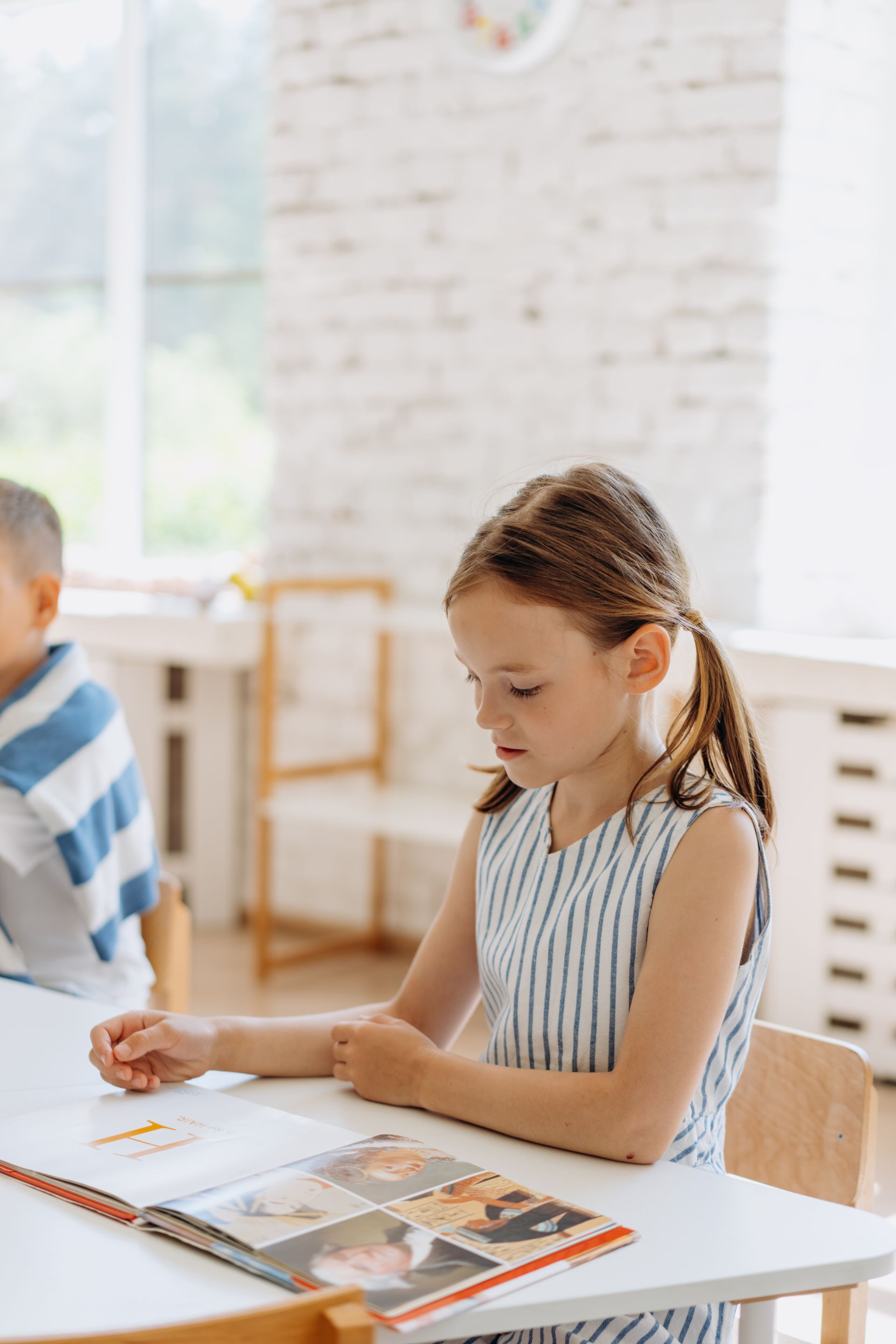 A focused young girl reading a book in a bright classroom setting