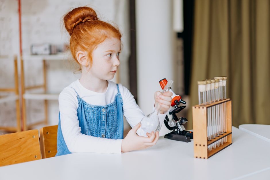 A young girl explores science with test tubes and microscopes in a bright indoor setting.