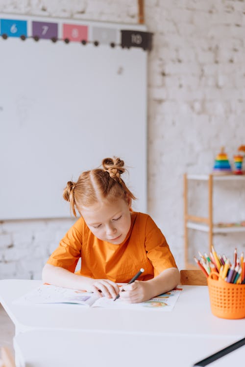 A Girl in Orange T-shirt Writing on the Book