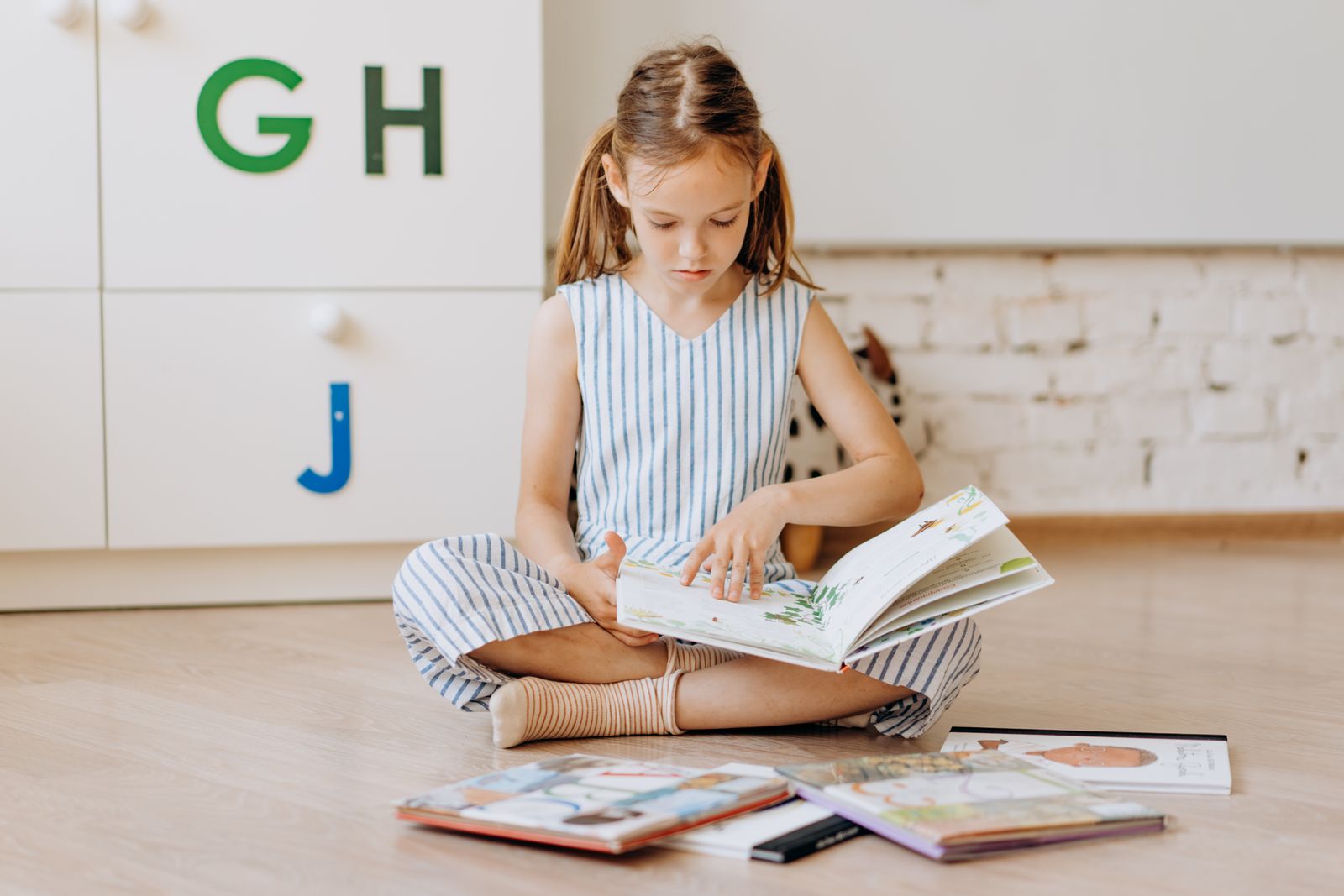 Дівчинка читає книжки, сидячи на підлозі