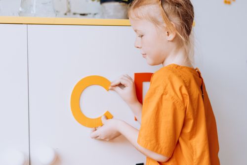 Free A girl in an orange shirt arranging colorful letters, promoting creativity and education. Stock Photo
