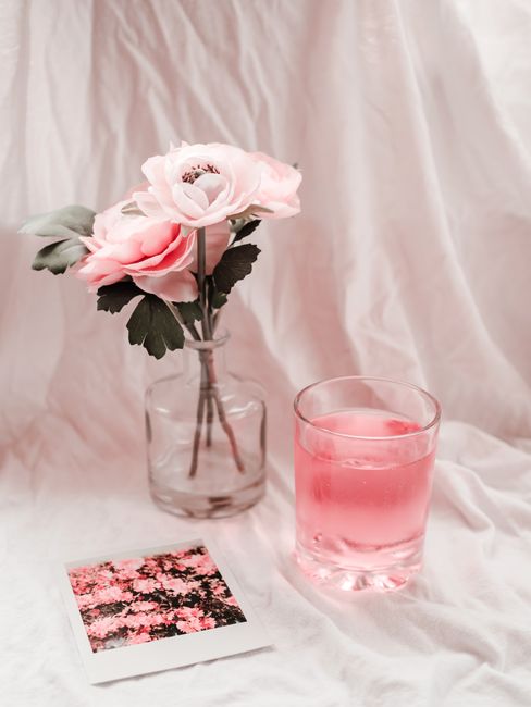 Delicate pink flowers in a vase alongside a pink beverage and photograph, exuding elegance and charm.