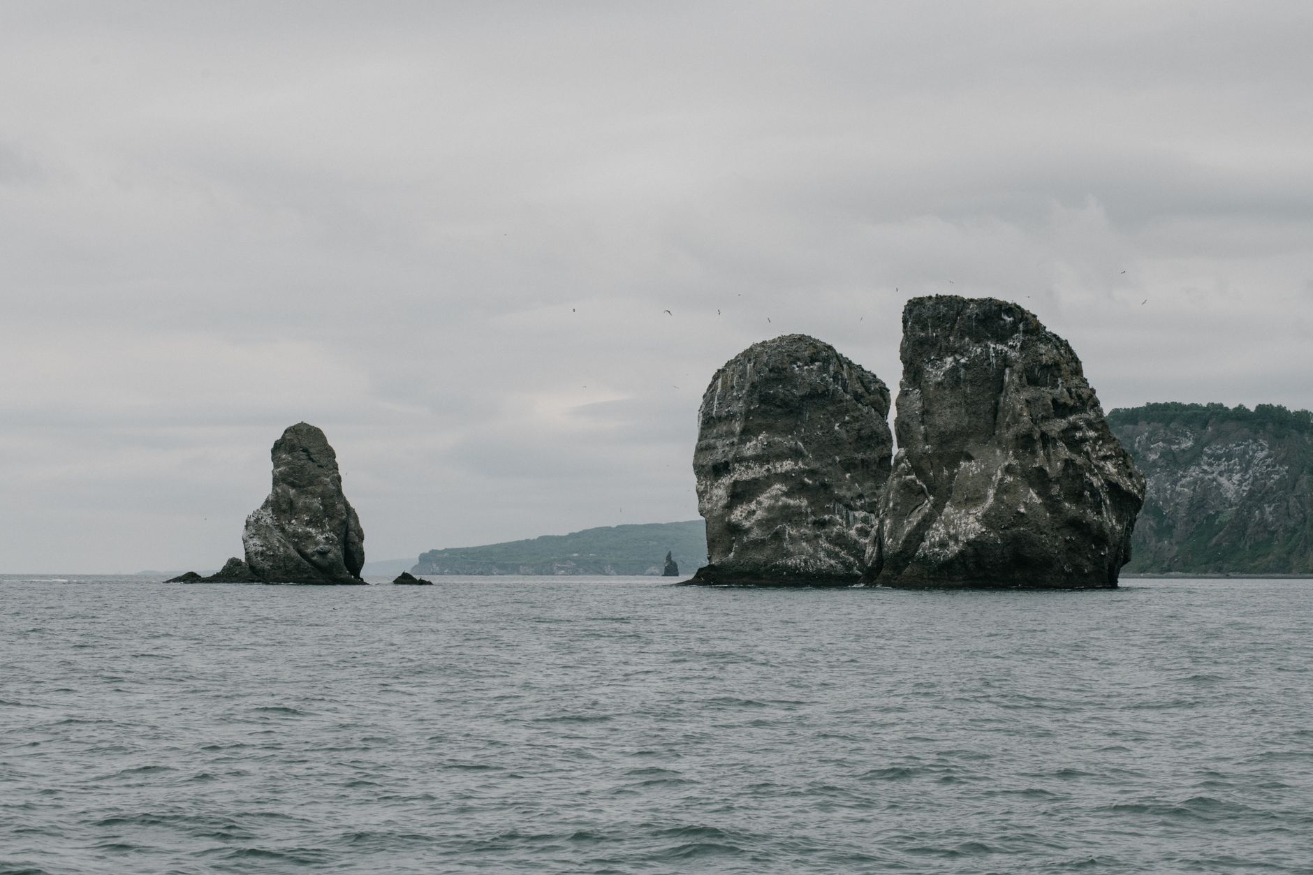 Moody grayscale view of the iconic Three Brothers rocks in Kamchatka, Russia's coastal waters.