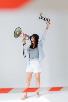 Asian woman energetically protesting with a megaphone and stop sign, barefoot and dynamic in a bright setting.