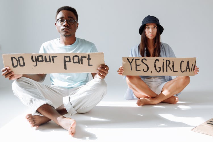 A Man And A Woman Sitting On Floor Holding Placards