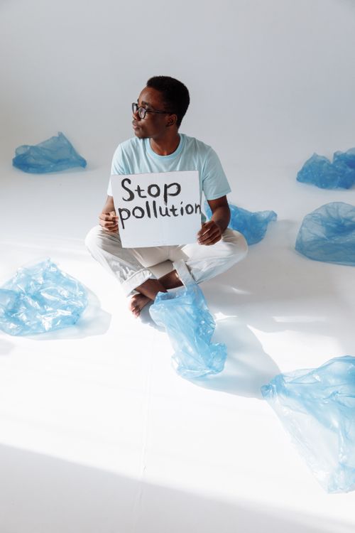 Free Man holding sign 'Stop pollution' among plastic bags, promoting environmental awareness. Stock Photo