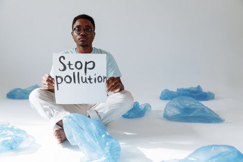 Free Man holding 'Stop pollution' sign surrounded by plastic bags, advocating environmental awareness. Stock Photo