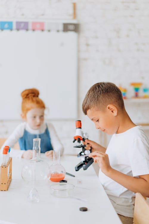 Boy Looking Into A Microscope Beside A Girl