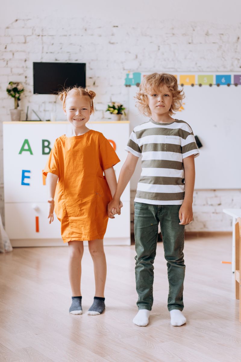 Dua anak berpegangan tangan di ruang kelas yang berwarna-warni.