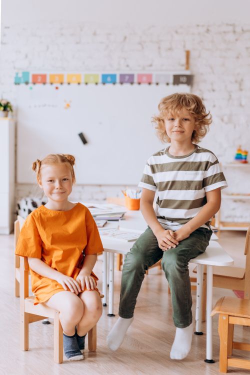 Free Two children sitting and smiling in a bright, elementary classroom. Stock Photo