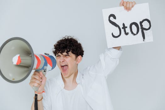 Person passionately expressing a protest message using a megaphone and a 'Stop' sign.