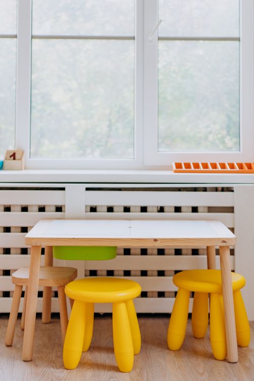 Free Colorful children's play area featuring a wooden table and stools by a sunny window. Stock Photo