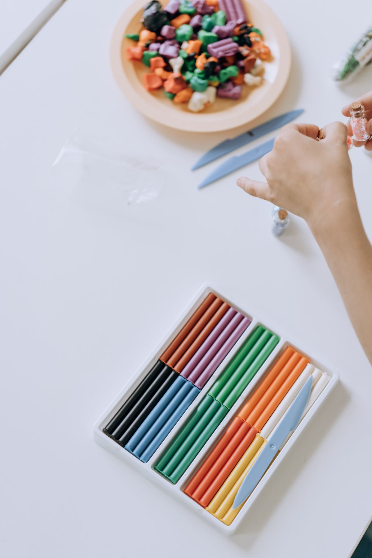 A child's hand holding bright sticks of colorful clay for rolling beads