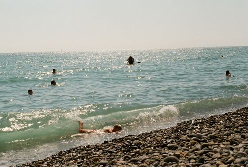 Free People enjoying a sunny day swimming in the ocean at a pebble beach. Stock Photo