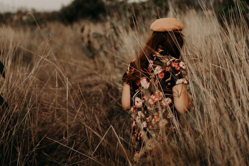 A Woman in Floral Dress Walking on Brown Tall Grass Field
