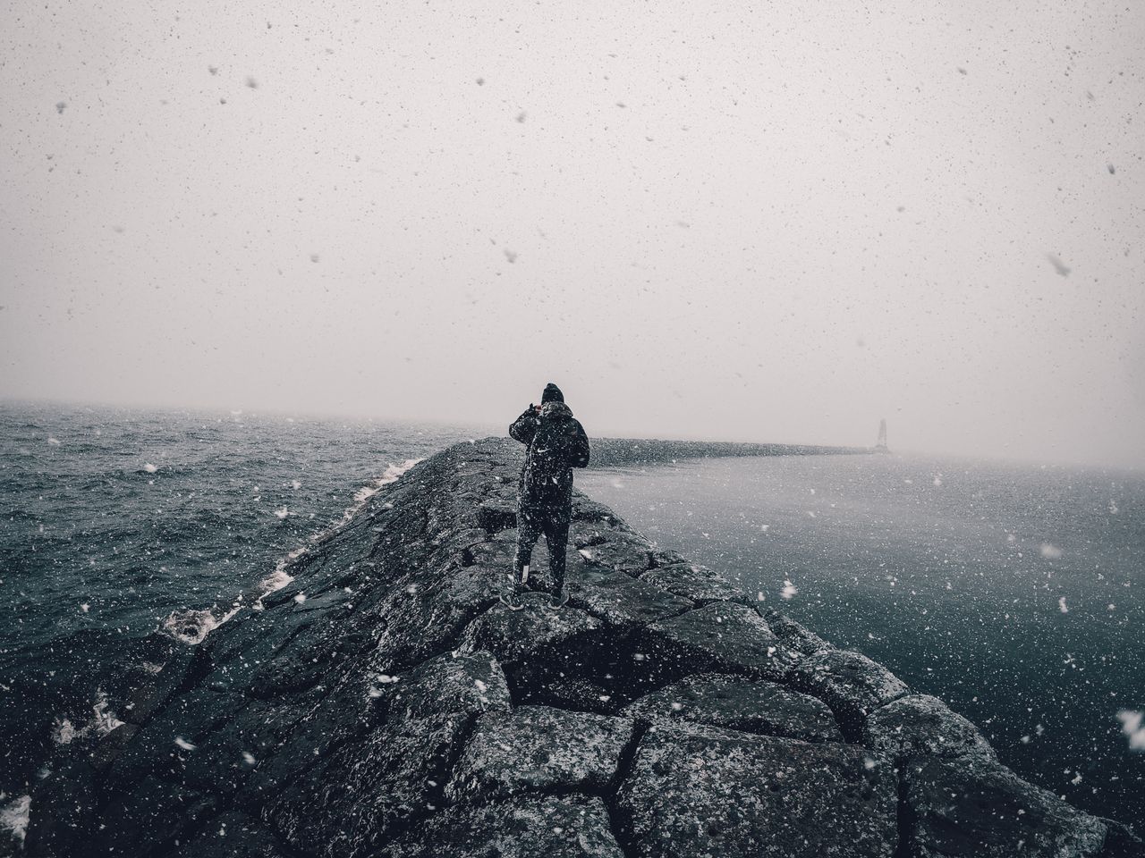 a person walks along a breakwater during a snowy day by the sea creati