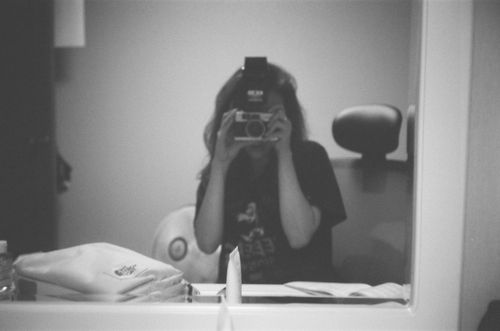 Free A grayscale self-portrait of a woman capturing herself in the mirror with a camera. Stock Photo