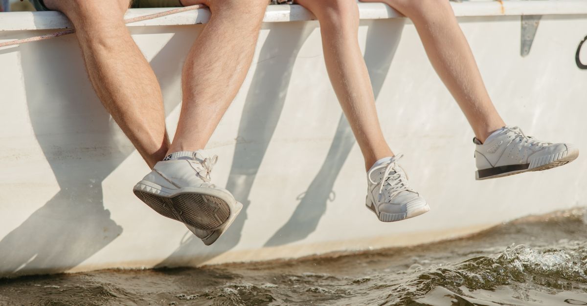 Casual scene of two people sitting on a boat, feet dangling over the water. Perfect for summer lifestyle themes.
