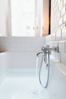 A modern white bathtub with chrome faucet and running water in a stylish tiled bathroom.