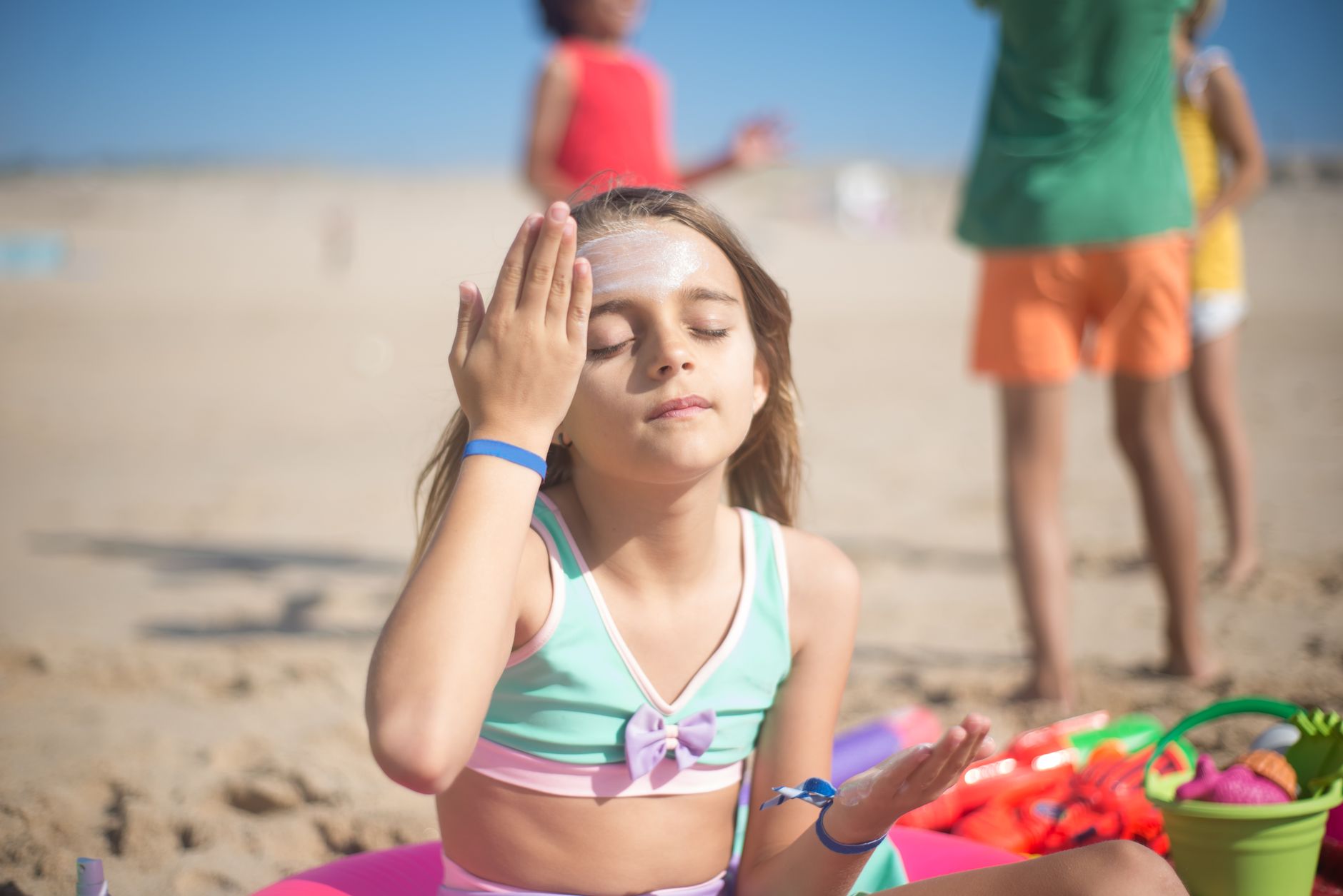 A young girl applies sunscreen on a sunny beach, enjoying a relaxing summer day.