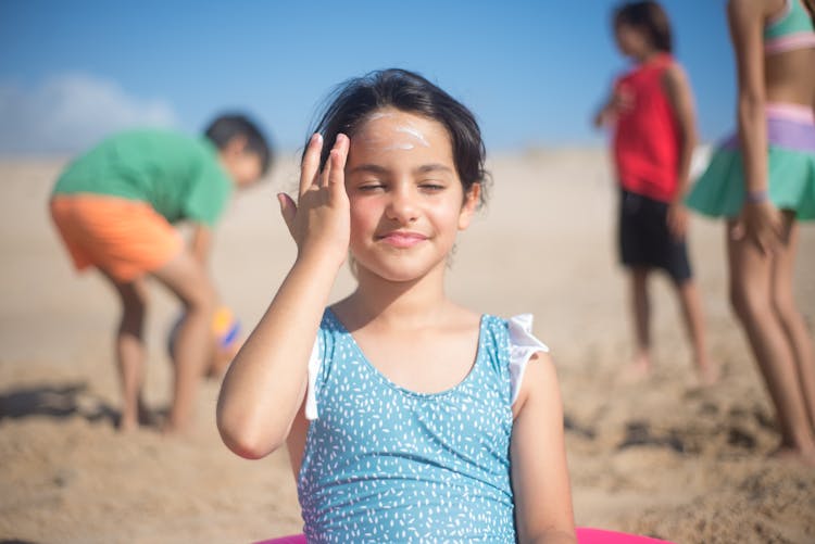 Child In Blue Swimsuit Applying Sunscreen On Face