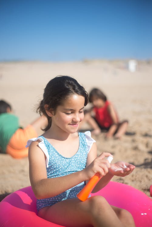 Free Young girl applying sunscreen while sitting on the beach during summer. Perfect protection for a sunny day. Stock Photo