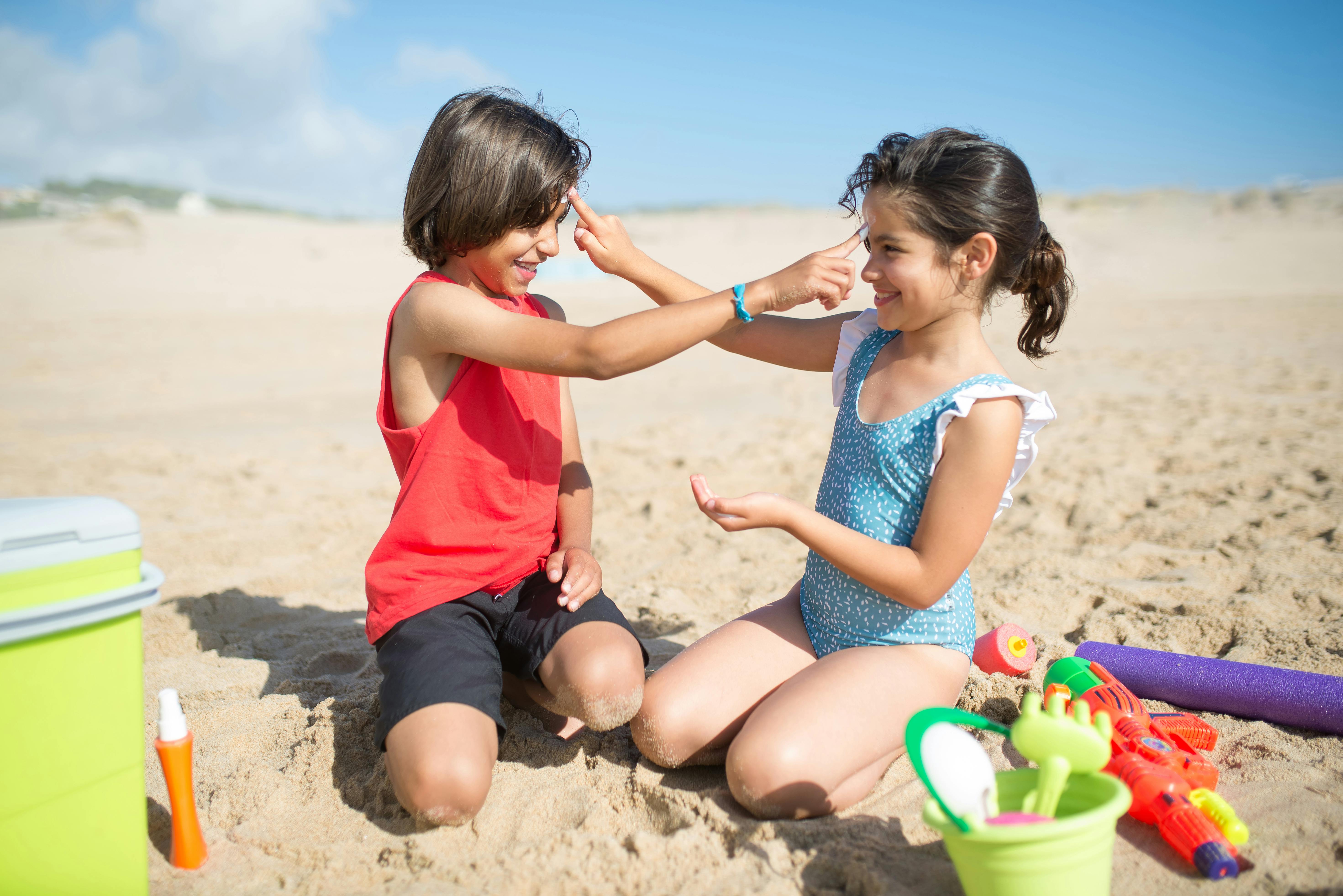 Children playing on a sunny beach, applying sunscreen and having fun with toys.