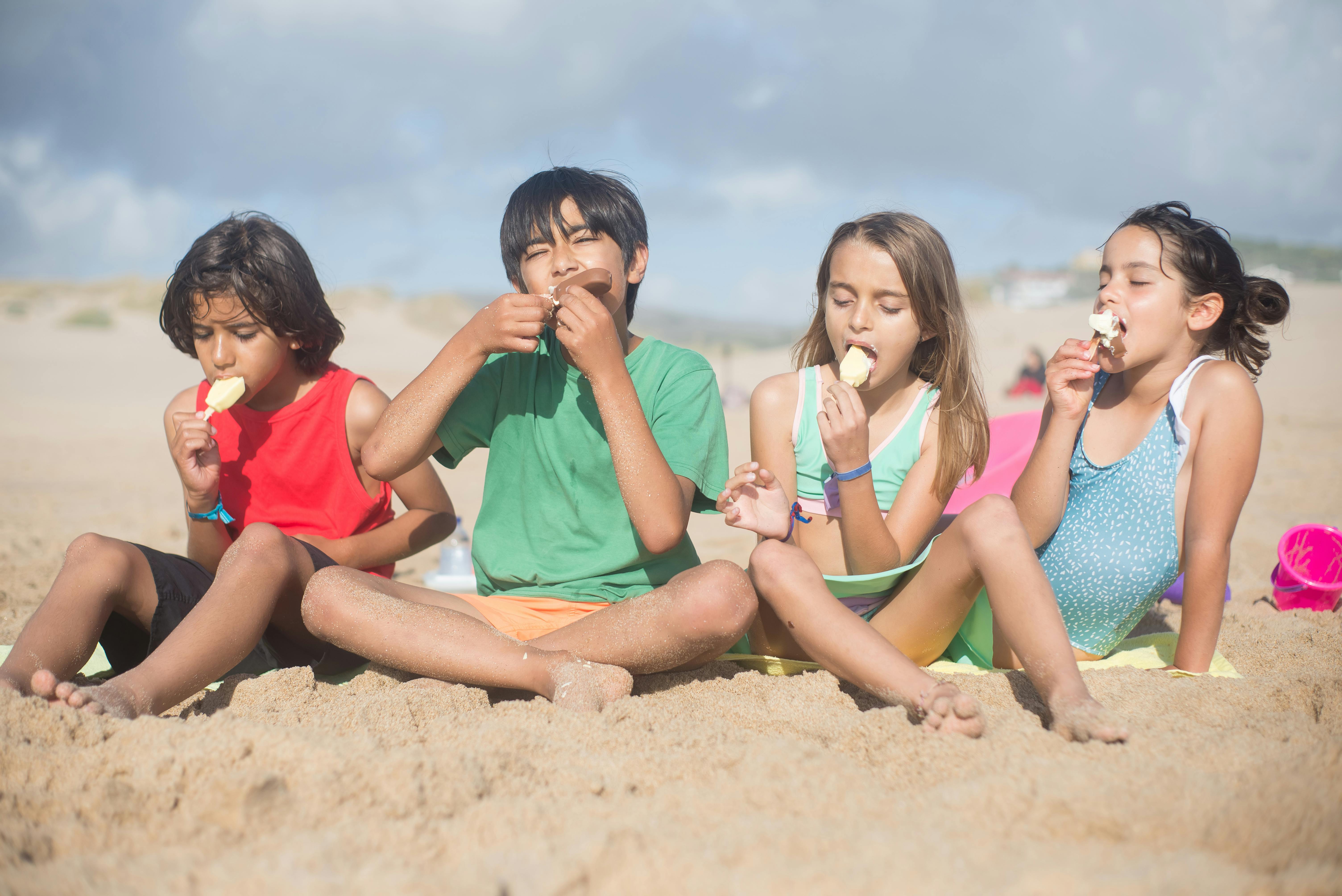 kids sitting on the sand eating ice cream stick