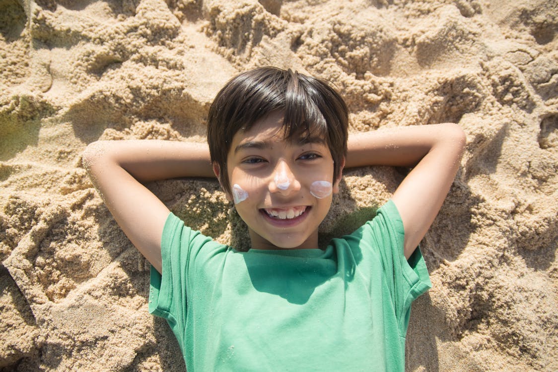Free A Boy with White Cream on the Face Lying on the Sand Stock Photo