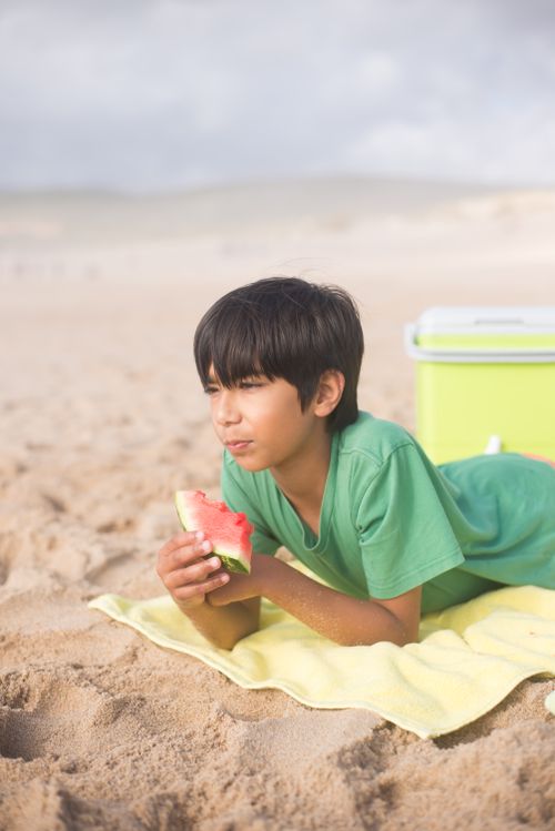 Free Child enjoying watermelon on a beach in Portugal, lying on a towel during a sunny summer day. Stock Photo